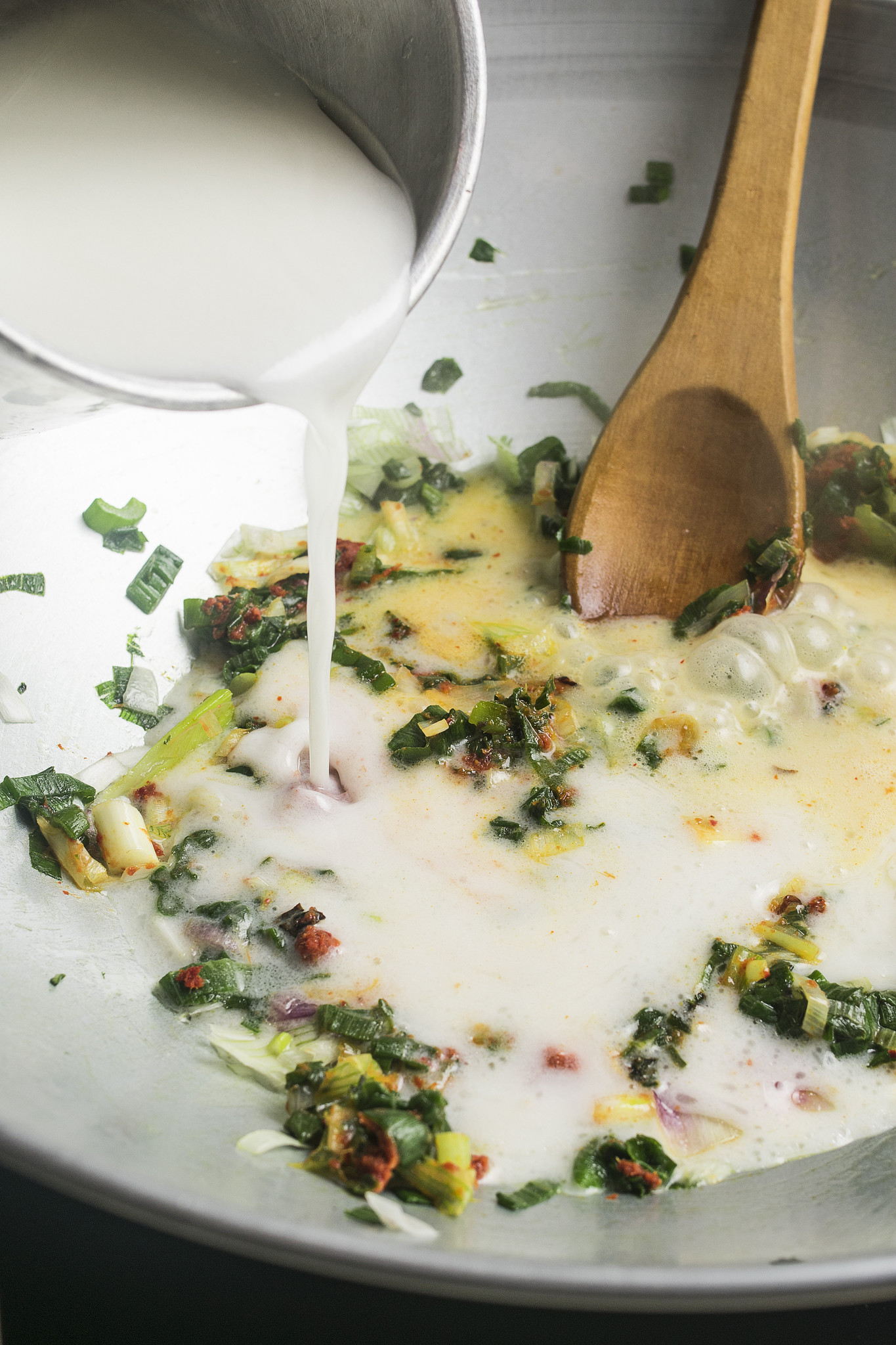 Coconut milk being poured into red Thai curry paste and spring onions in a wok.